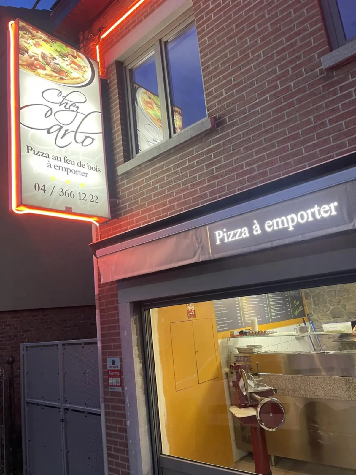 L’enseigne lumineuse de Chez Carlo rue de Herve, le soir : pizza au feu de bois à emporter.