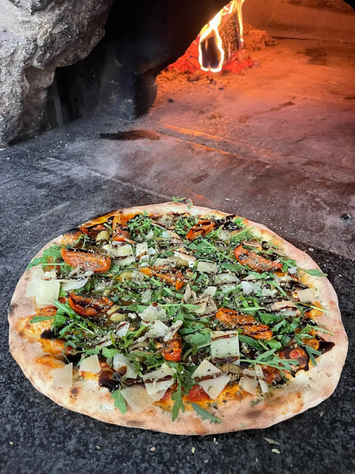 Une pizza garnie de roquette, de copeaux de parmesan et d’un filet de balsamique, à la sortie du four.